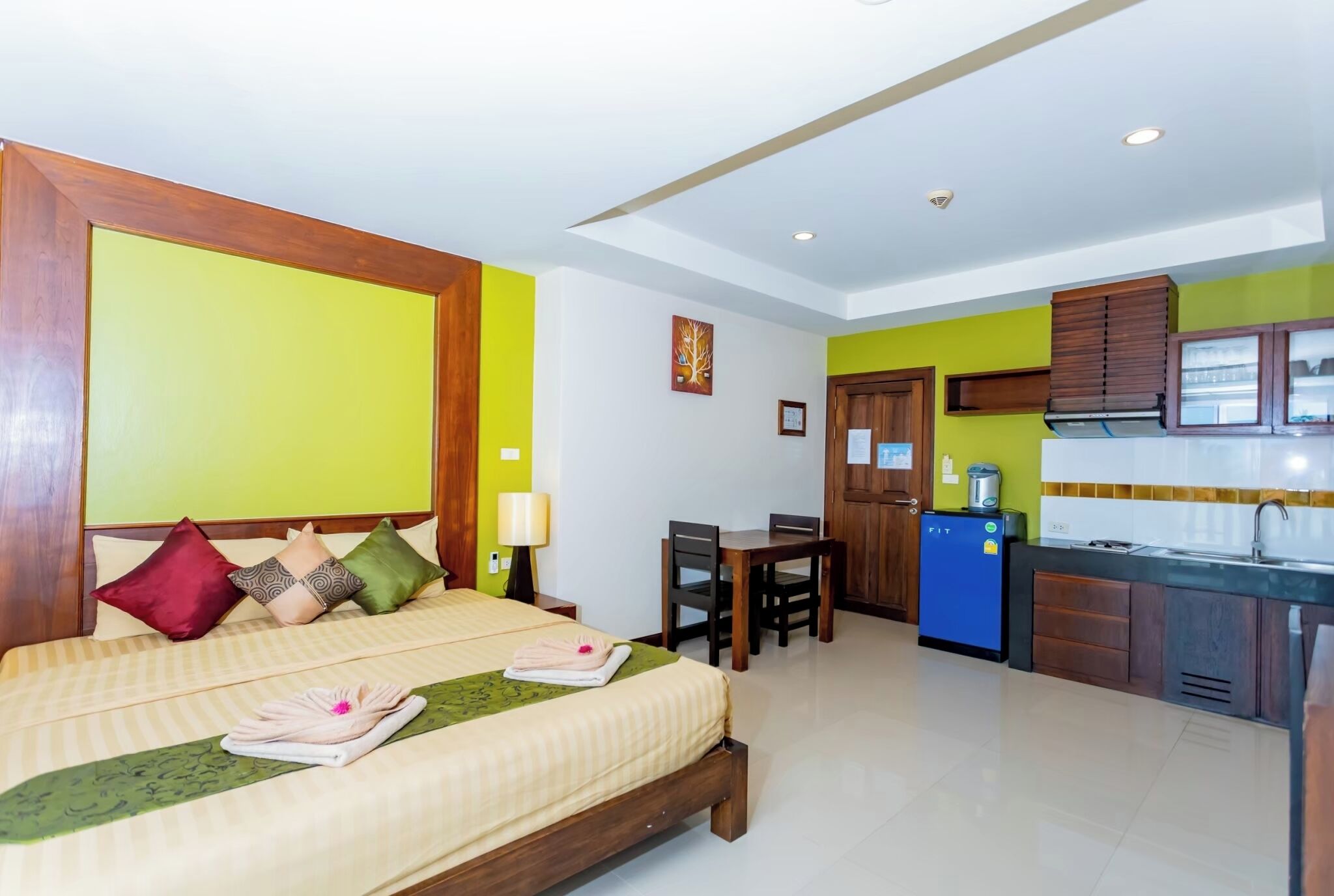 A hotel room with a bed, bedside table, lamp, and a small kitchenette.