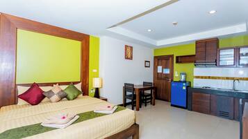 A hotel room with a bed, bedside table, lamp, and a small kitchenette.