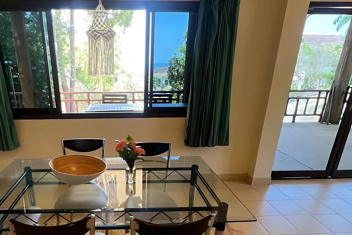 A dining area with a glass table, four chairs, a bowl, and a vase with flowers.