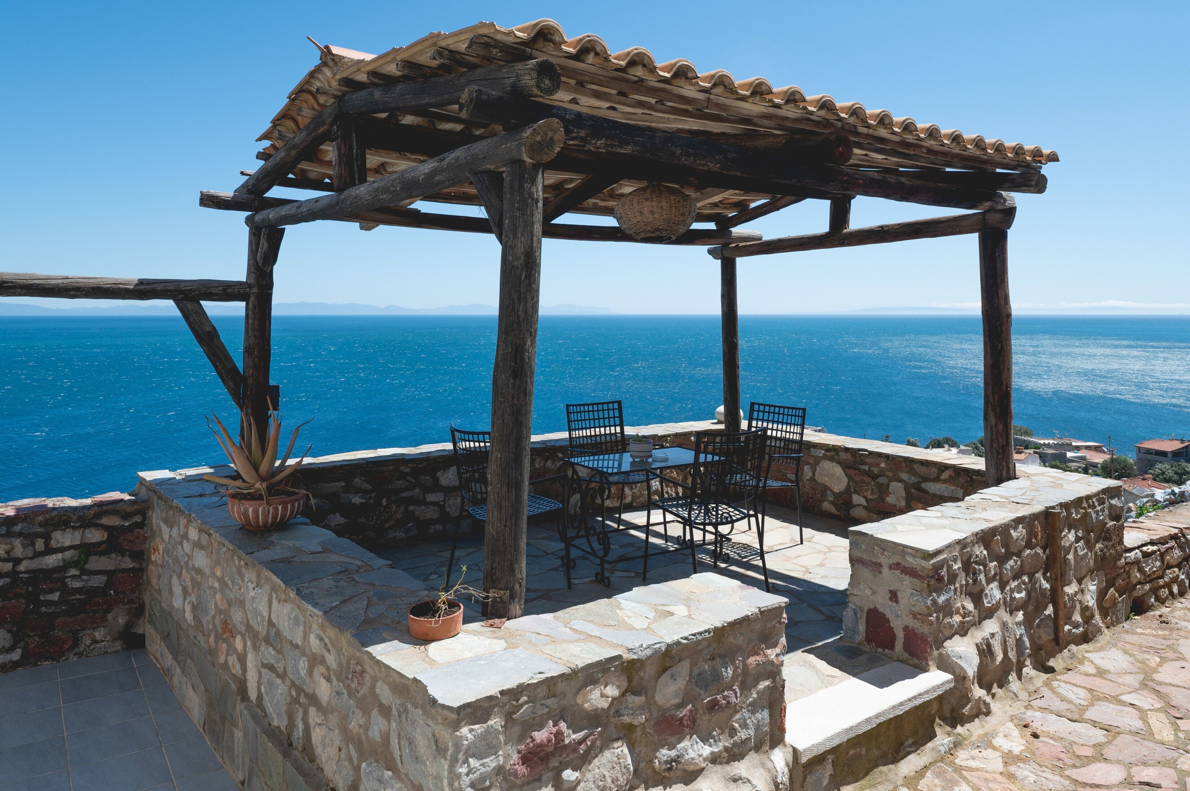 A wooden pergola with a table and chairs overlooking the sea.
