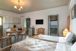 A room with two beds, a dining table, chairs, a TV, and a view of the sea.