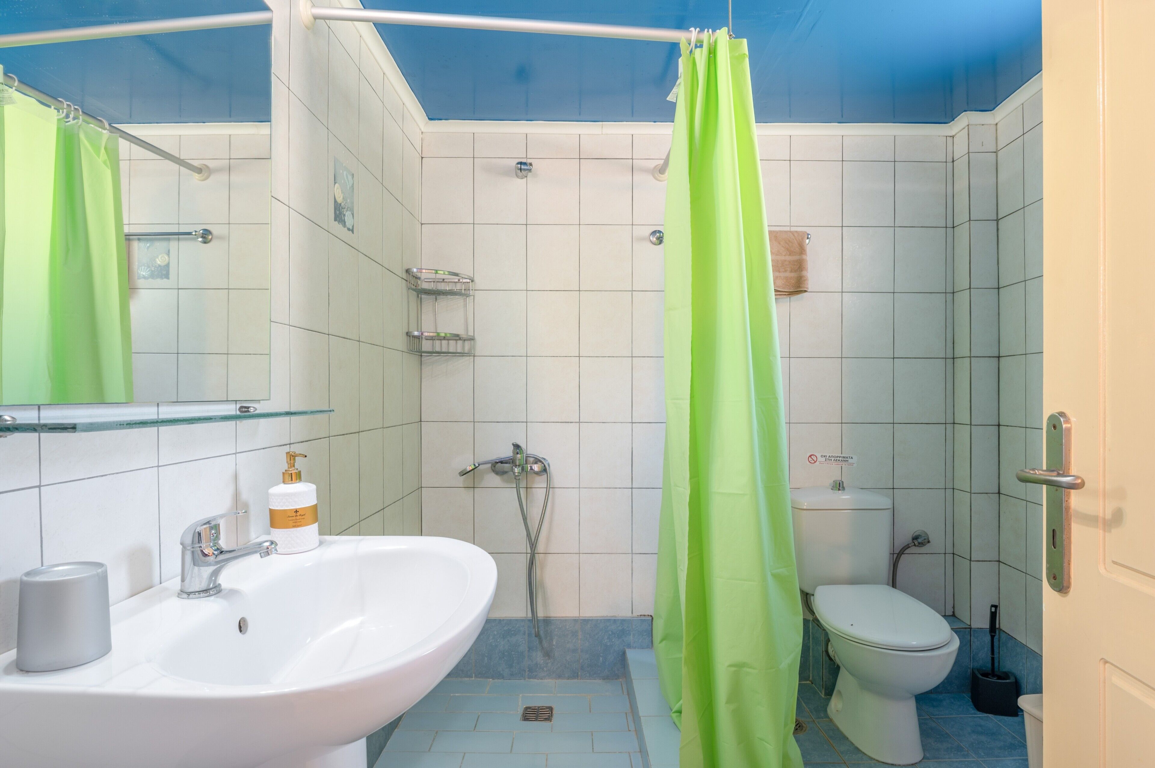 A bathroom with a white sink, a shower, a toilet, and a green shower curtain.