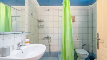A bathroom with a white sink, a shower, a toilet, and a green shower curtain.