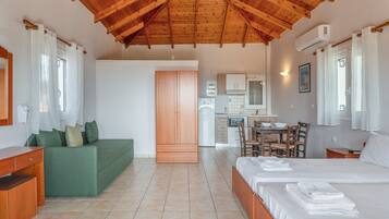 Quarto com teto de madeira, sofá verde, cama com toalhas, cozinha e mesa de jantar.