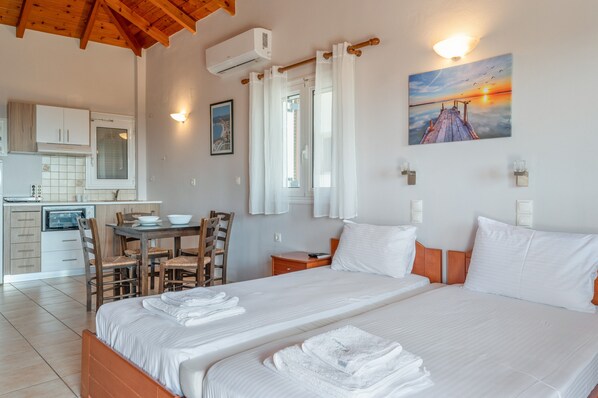 A hotel room with a bed, a desk, a chair, a small table, and a kitchen area.