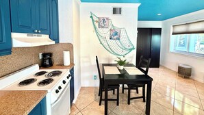 A kitchen with a stove, coffee maker, and a dining table with chairs.