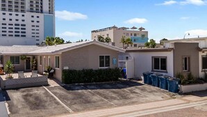 A residential area with a small house, paved driveway, and a tall building in the background.