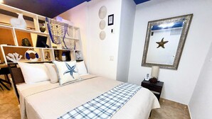 Une chambre d’hôtel avec un lit, un bureau et une chaise. On y trouve une étagère avec divers objets et un miroir au mur.