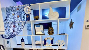 Une pièce avec un meuble blanc, une étagère ornée d’une pancarte de bienvenue, un certificat encadré, un filet décoratif et une étoile de mer.