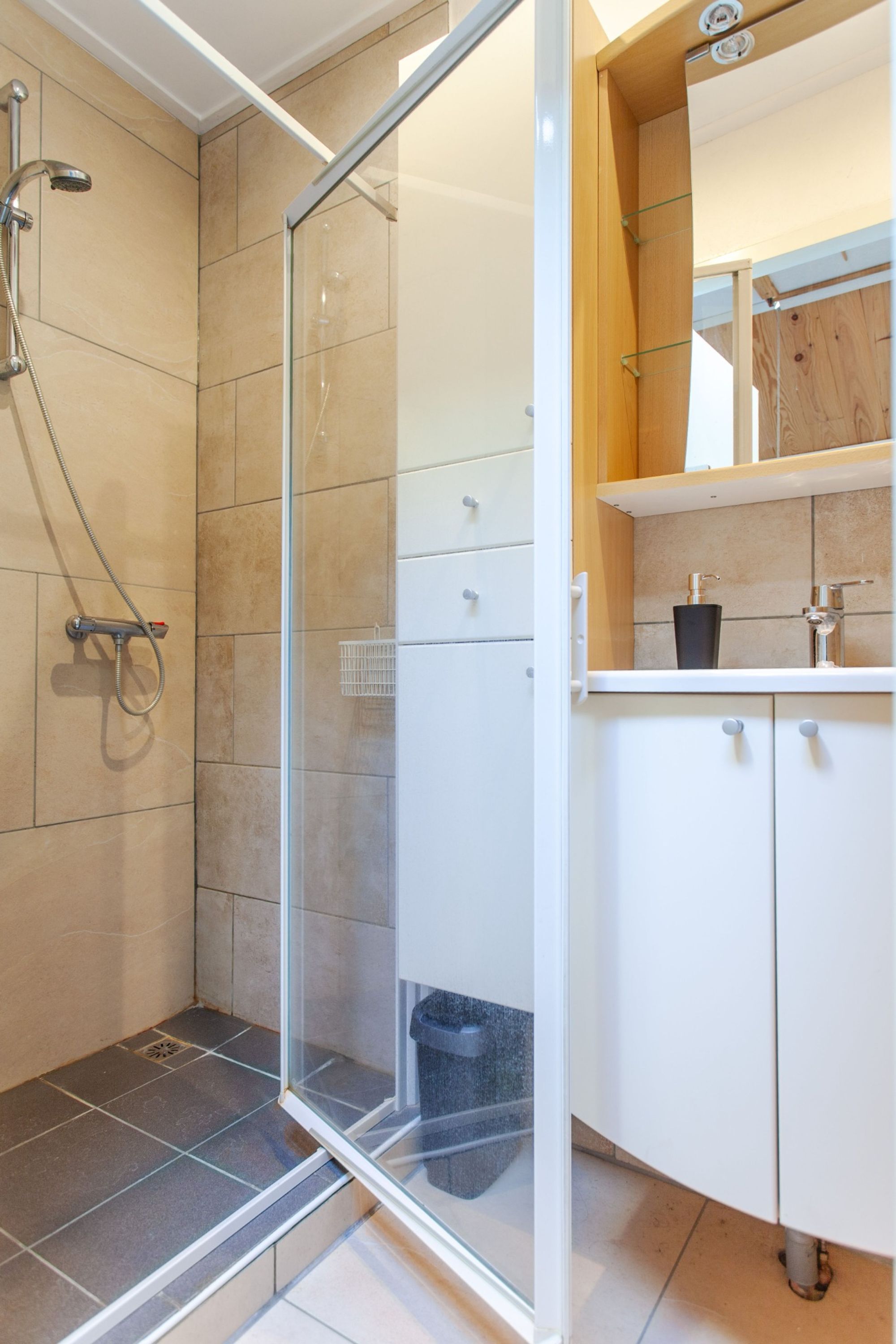 Ein modernes Badezimmer mit Duschkabine aus Glas, weißen Schränken und einem Holzausziehtisch.