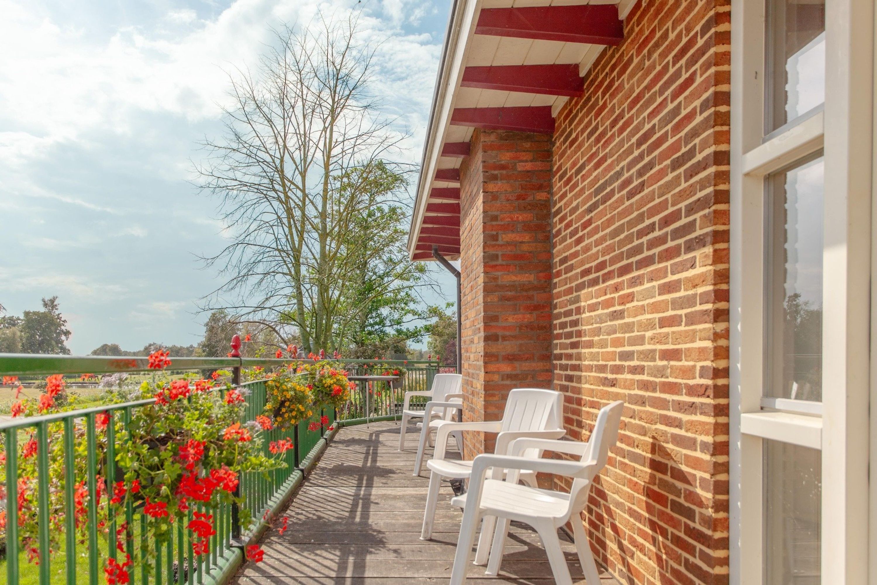 A balcony with a brick wall, white chairs, and a green railing with flowers.