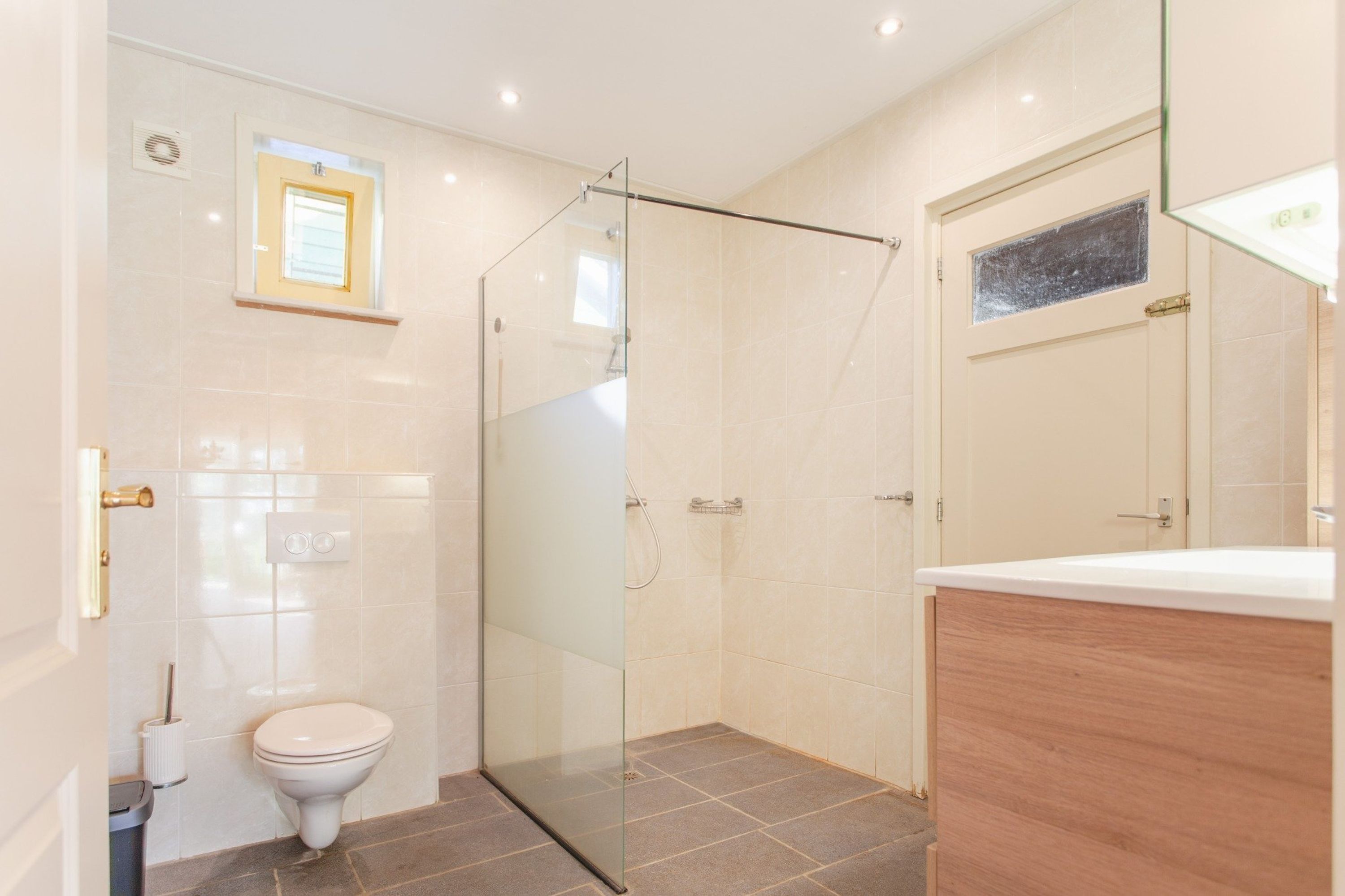Un baño moderno con cabina de ducha de vidrio, inodoro y tocador de madera.