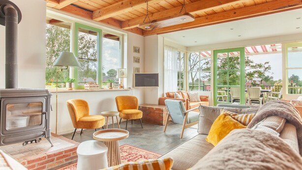 A cozy living room with a fireplace, comfortable seating, and large windows offering a view of the outdoors.