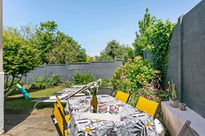 Eine Terrasse im Freien mit Tisch für zwei Personen, umgeben von Grünpflanzen und einem Holzzaun.