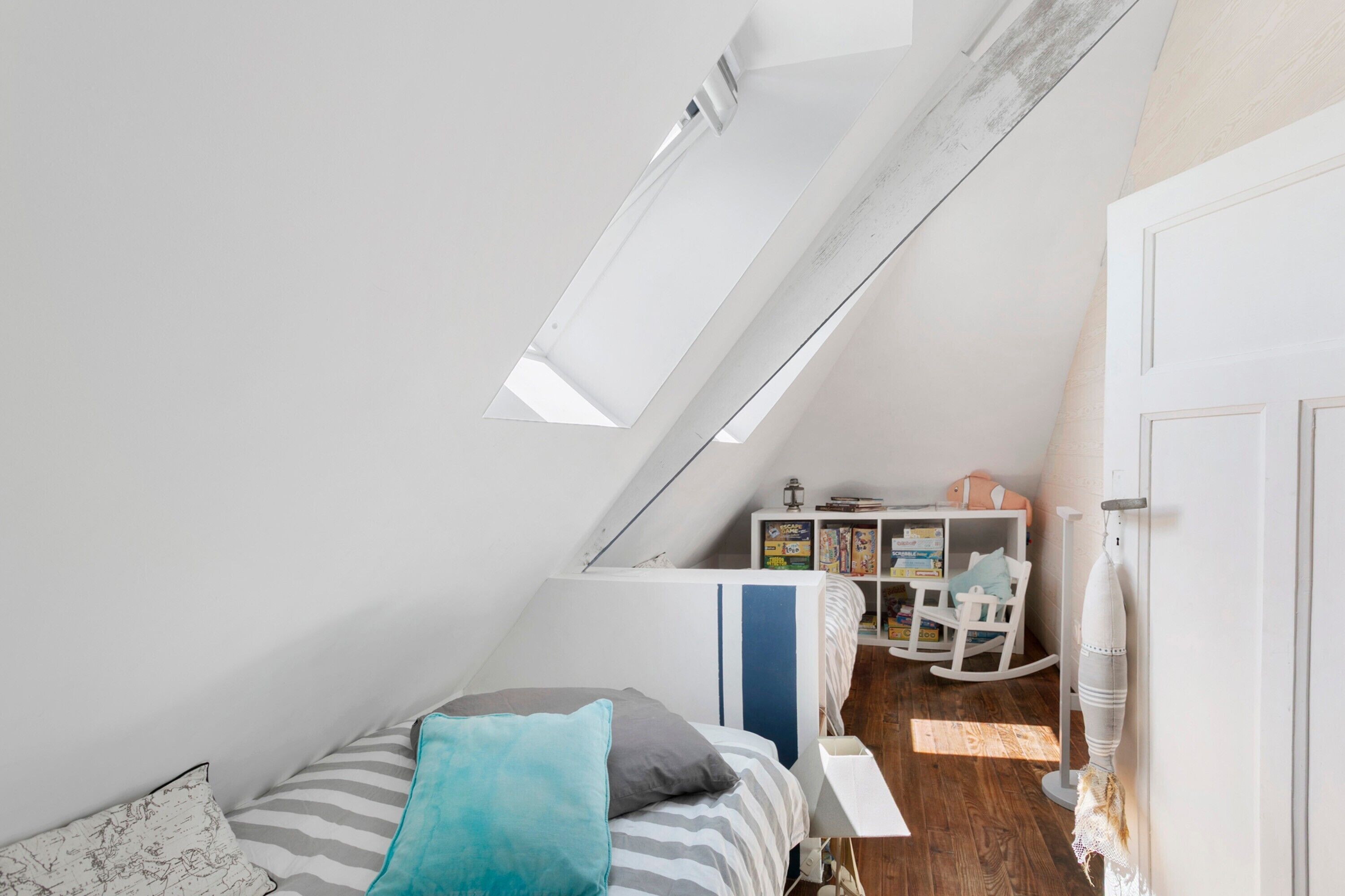 A bedroom with a sloped ceiling, a bed with striped bedding, a small desk with a chair, and a bookshelf.
