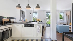 A modern kitchen with a central island, pendant lighting, and a view to a living area.