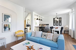 Un salon moderne avec un canapé bleu, une table basse et une cuisine en arrière-plan.