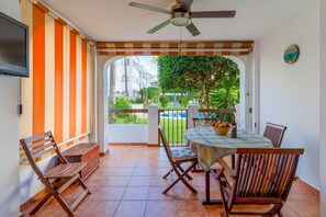 A patio with a table and chairs, a ceiling fan, and a view of a swimming pool and greenery.