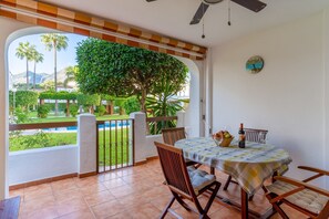 A balcony with a table, chairs, a clock, and a view of a garden and pool.