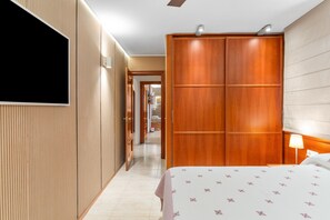 A hotel room with a bed, a wardrobe, a television, and a hallway leading to another room.