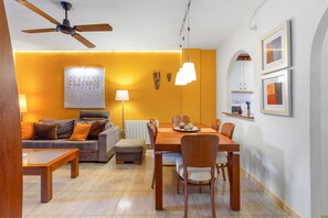 En moderne stue med sofa, spisebord, stole, loftventilator, lampe og billeder på væggen.