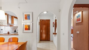 Een gang met een houten deur, kunstwerken in de lijsten aan de muur en een eetgedeelte met een tafel en stoelen.
