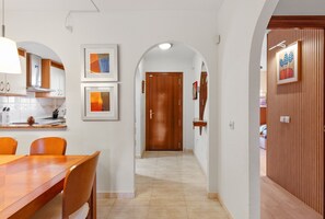 A hallway with a wooden door, framed artwork on the walls, and a dining area with a table and chairs.