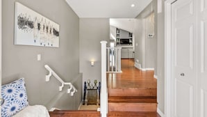 A staircase leading to a kitchen area with a white railing, a wall-mounted abstract painting, and a decorative table with candles.