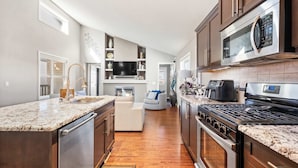 A modern kitchen with a central island, built-in oven, microwave, and a large TV.