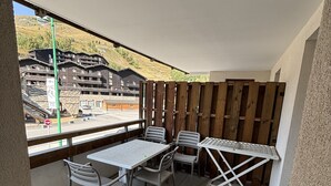 A balcony with a table and chairs, a view of a mountain resort, and a stop sign in the background.
