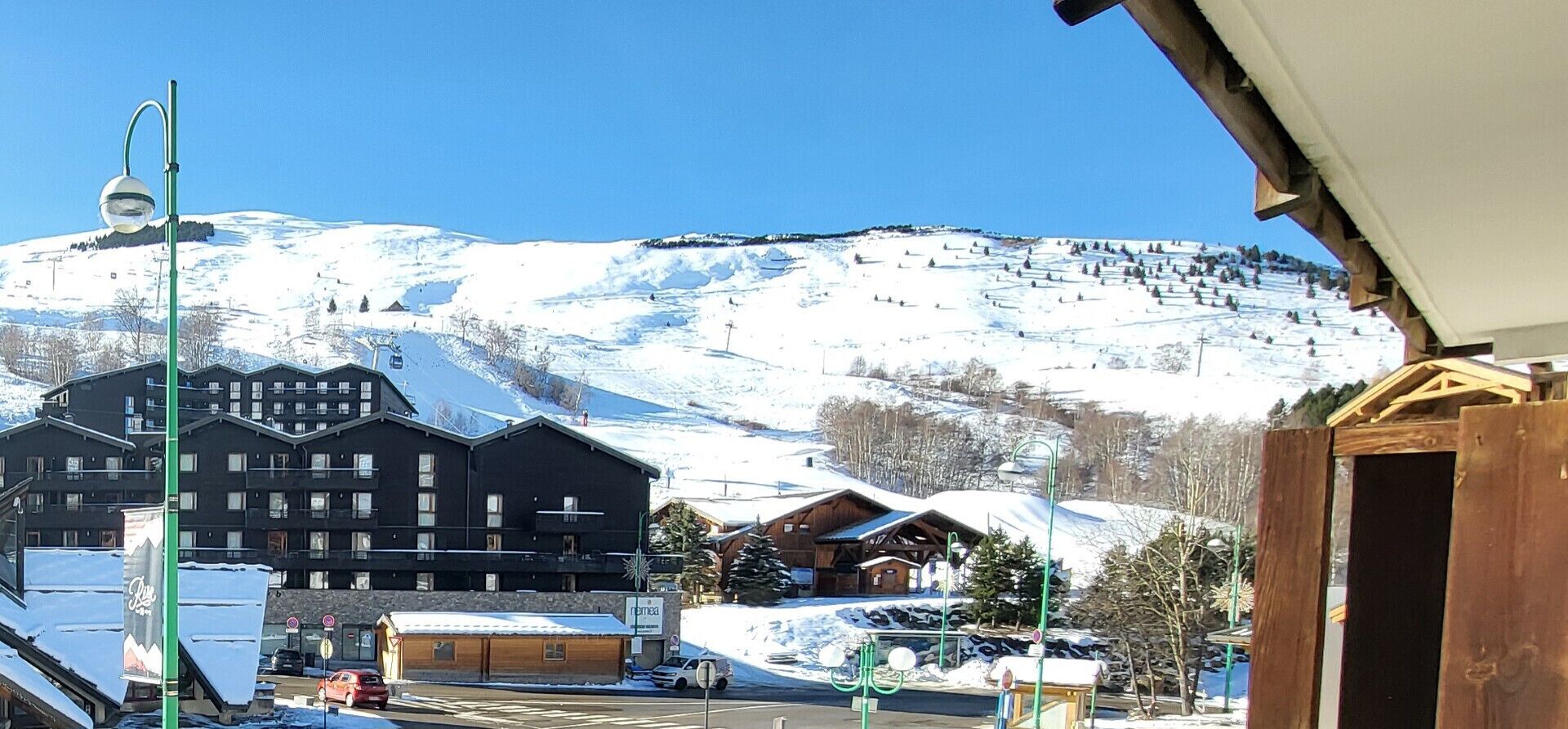 A snow-covered mountain with a ski resort in the background, a building with a sign, and a street with parked cars.