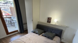 A bedroom with a bed, a bedside table with a lamp, a window with curtains, and a view of the outside.