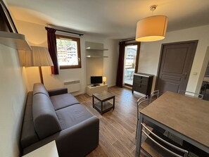 Ein kompakter Wohnbereich mit Sofa, kleinem Tisch, Fernseher, Lampe und Essbereich.