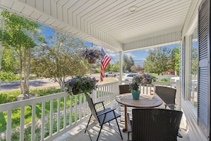 A covered porch with a table and chairs, an American flag, and hanging flower baskets.