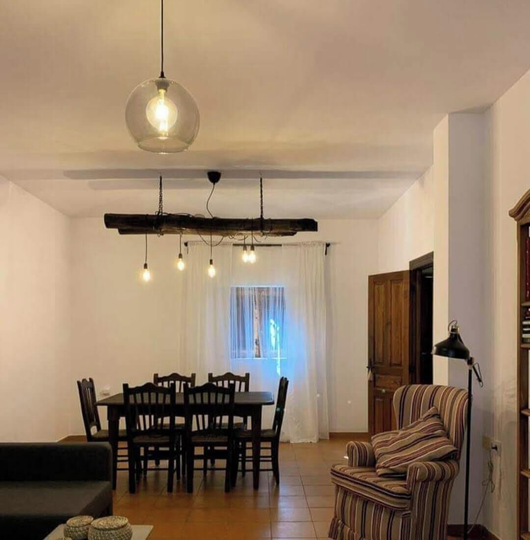 A dining area with a wooden table and chairs, a striped armchair, and a hanging light fixture.