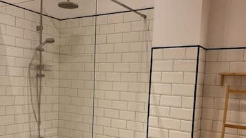 A shower with a glass door, white tiled walls, and a wooden ladder.