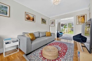 A living room with a grey sofa, a white side table, a woven ottoman, and a large patterned rug.