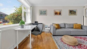 A modern living room with a grey sofa, a white table, and a large window with a view of greenery.
