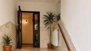 Uma escadaria de mármore com corrimão, plantas em vasos e um radiador na parede.