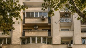 Um edifício de vários andares com entrada central, varandas e unidades de ar condicionado.