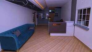 Un área de recepción con un mostrador identificado con la etiqueta "RECEPTION", un sofá azul y piso de madera.