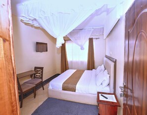 A hotel room with a bed, a desk, a chair, a TV, and a door.