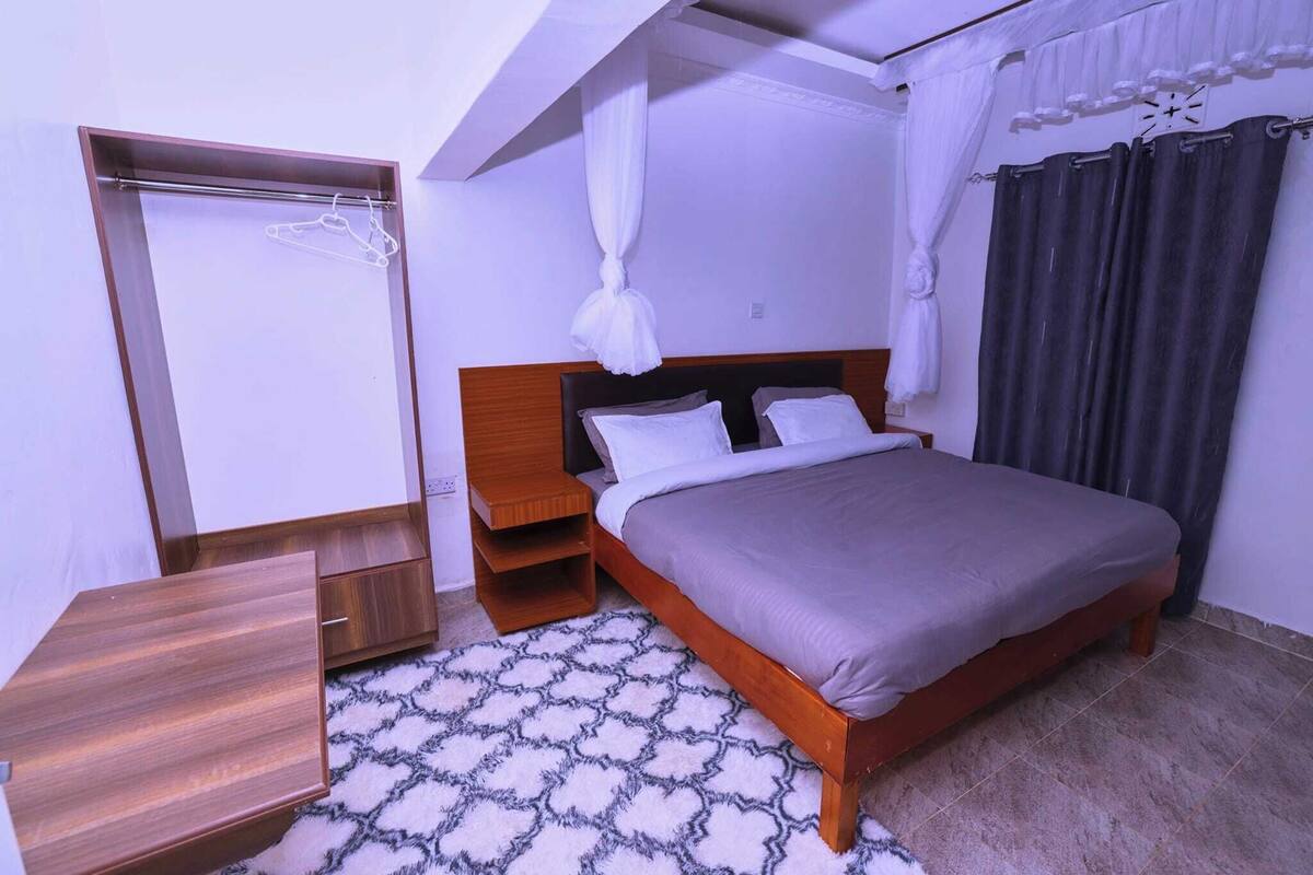 A bedroom with a bed, a wardrobe, a bedside table, and a patterned rug.