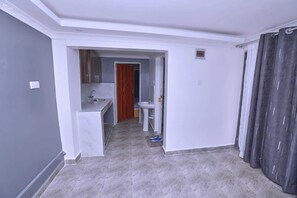 A hallway leading to a kitchen and bathroom with grey walls, white trim, and grey tiled flooring.