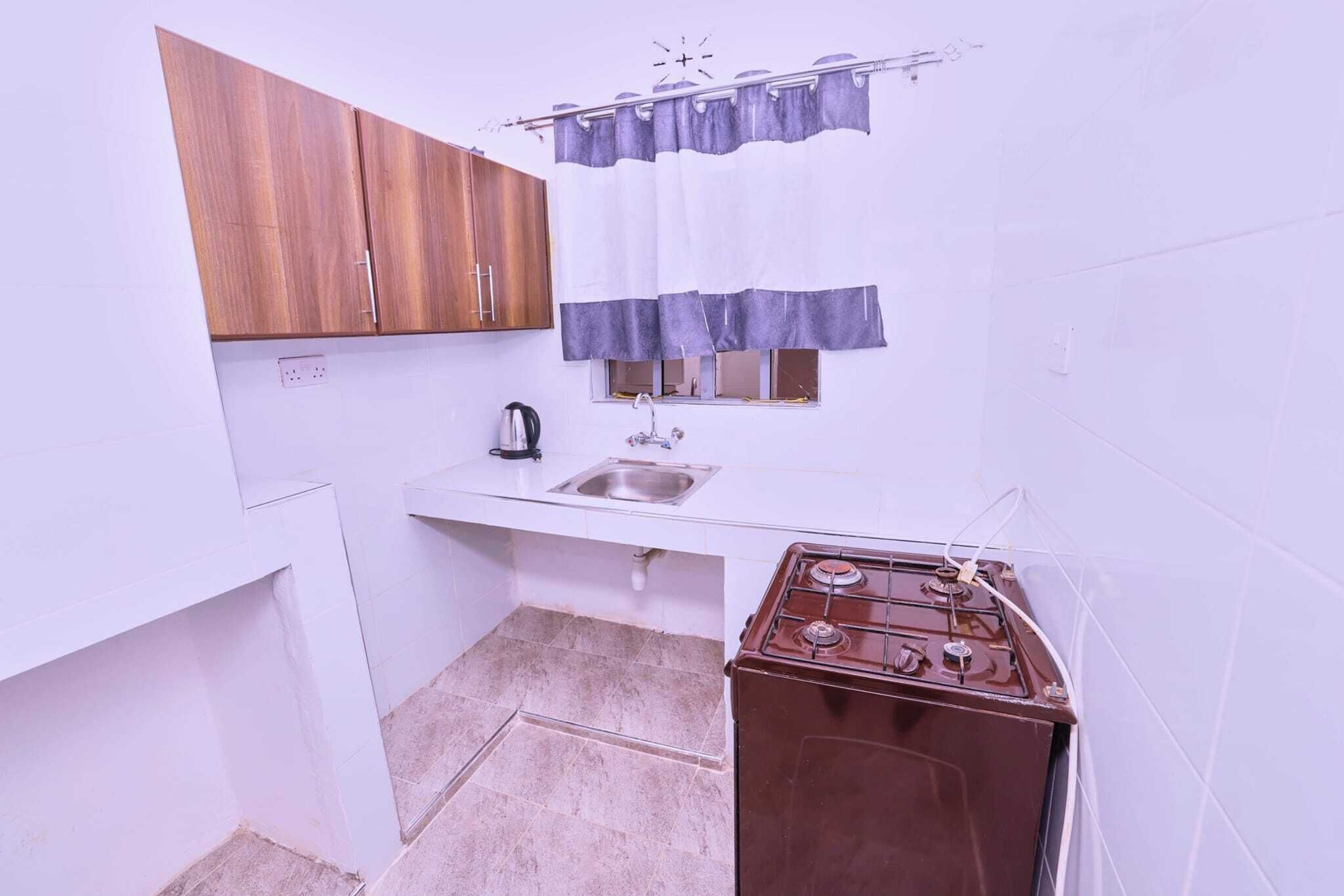 A compact kitchen with white walls, a wooden cabinet, a sink, a window with a curtain, and a stove.