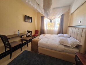 A hotel room with a bed, a desk, a chair, a TV, and a window with curtains.