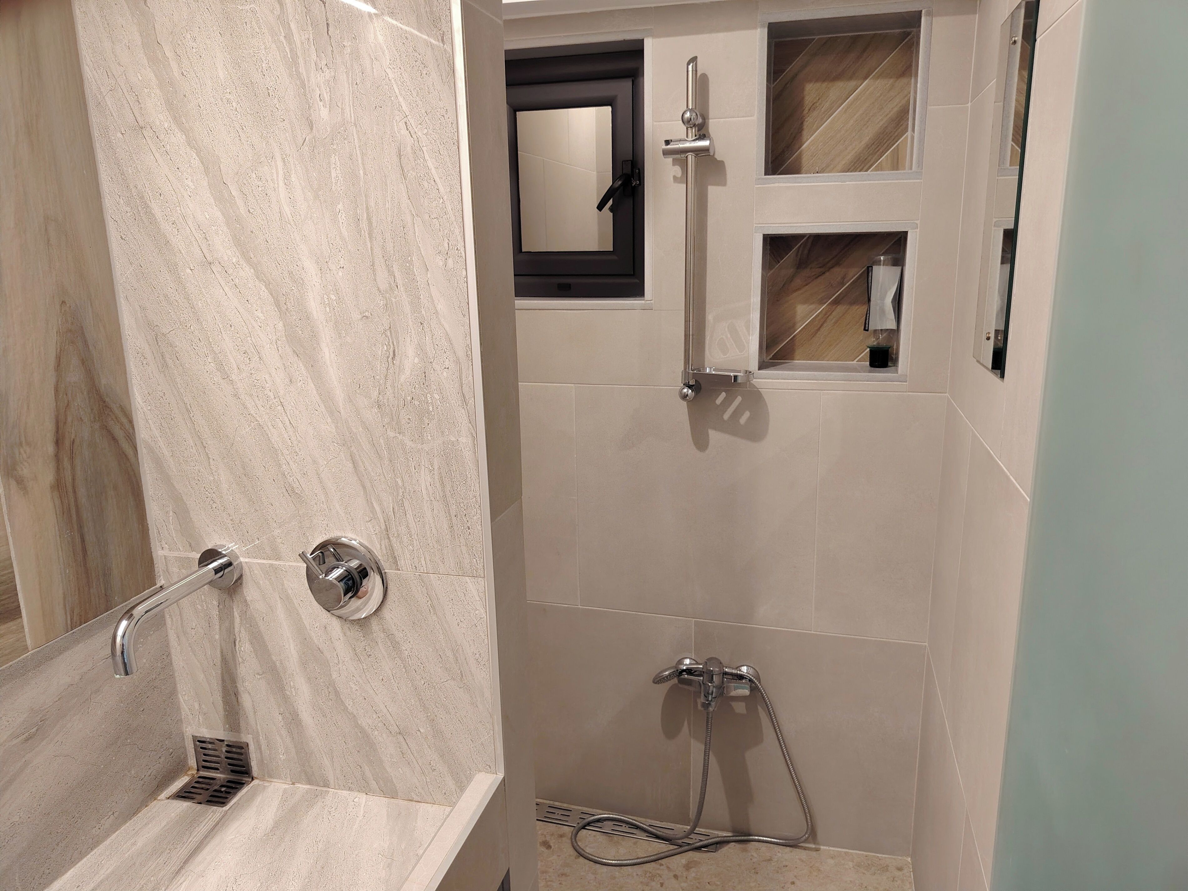 A bathroom with a marble sink, a shower with a handheld showerhead, and a mirror with a wooden frame.