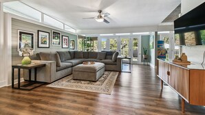 A spacious living room with a sectional sofa, a coffee table, and a TV on a wooden cabinet. - Tropical Lagoon w/ Private Pool & Game Room! (Clearwater)