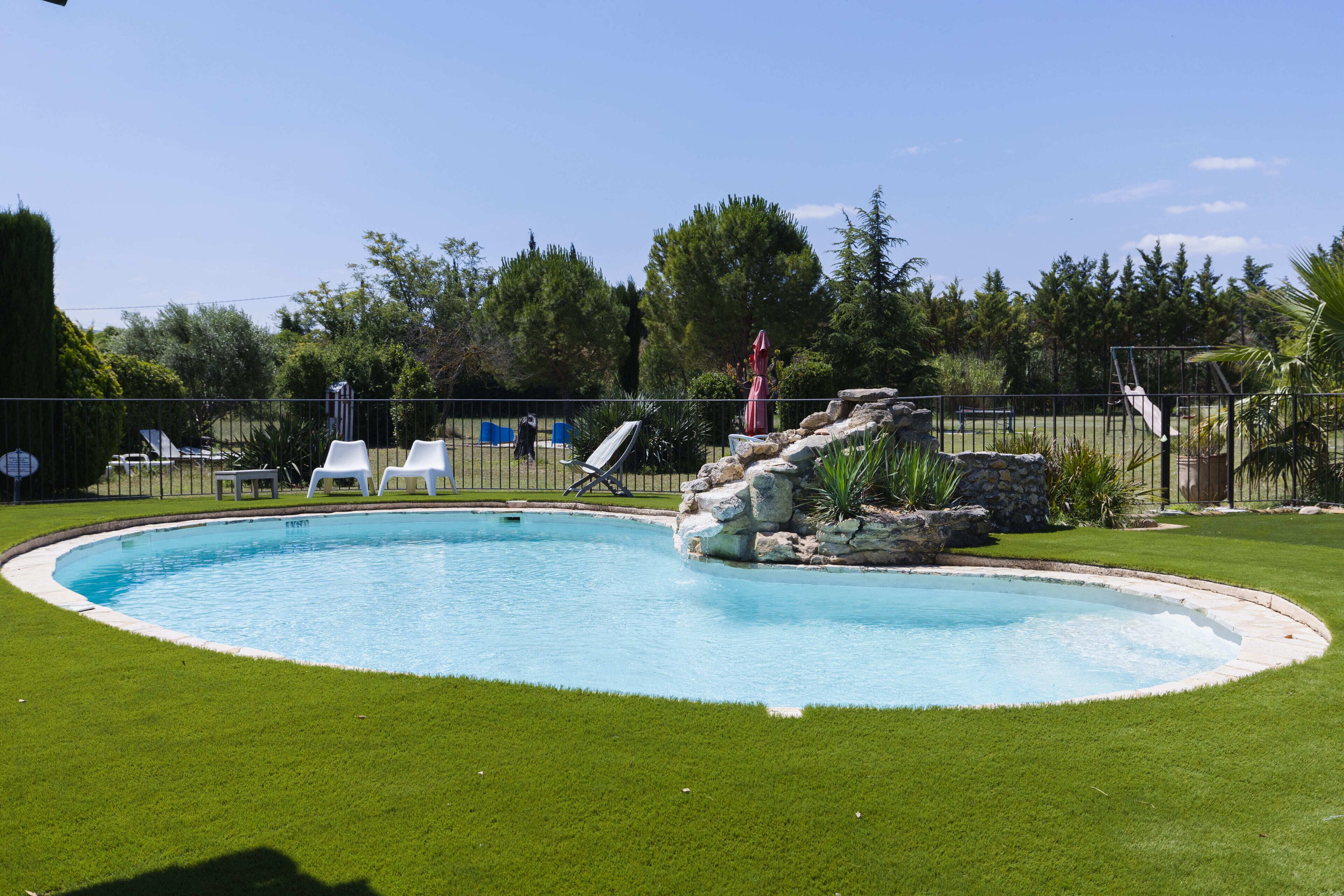 En swimmingpool med en klippformation som dekor, omgiven av en välskött gräsmatta och ett staket.