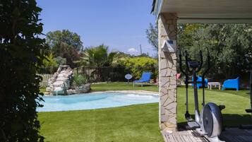 A backyard with a swimming pool, a patio area with exercise equipment, and a stone wall.